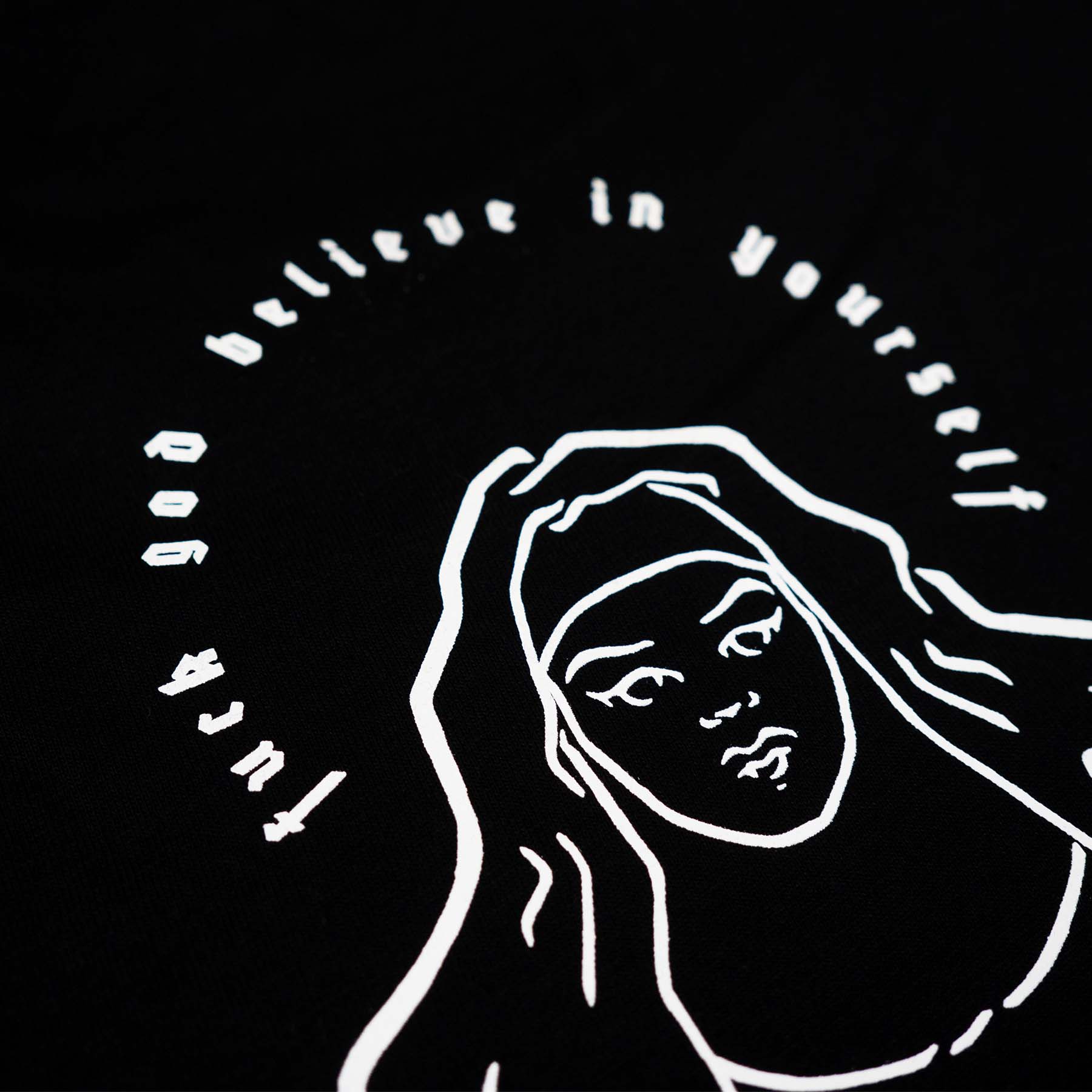 Close up of the naked nun with the text "fuck god believe in yourself" screen-printed in white colour on a black shirt on the whole back